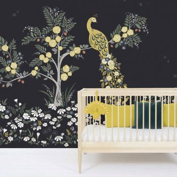 Ein Babybett aus hellem Holz mit gelb-schwarzen Kissen abgestimmt auf das Lilipinso-Wandbild mit Pfauenmotiv dahinter.
