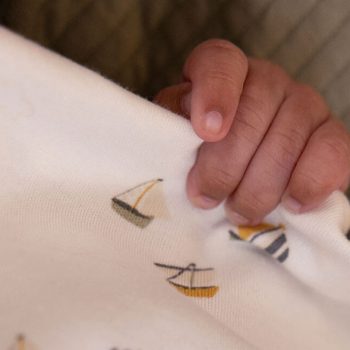 Eine Säuglingshand hält seine Bettdecke fest. Sie ist mit der Bettwäsche "Sailors Bay" von Little Dutch bezogen und zeigt kleine SChiffe in gelb und blau auf weißem Untergrund.