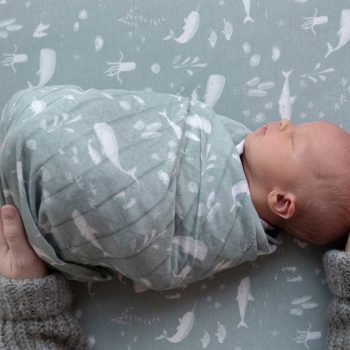 Ein Säugling ist gepuckt, also fest eingewickelt in ein Tuch von Little Dutch "Ocean Mint". Zwei Erwachsenen-Hände halten es schützend an Kopf und Füßen.