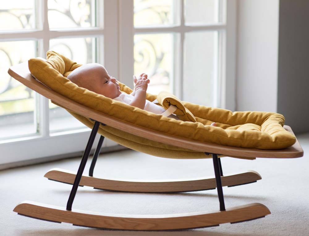 Ein Baby sitzt in einer safrangelben Babywippe von Quax. Vielleicht schläft es ja gleich ein!